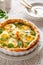 Quiche with with boiled eggs and leeks sprinkled with fresh lambs lettuce and dill served in casserole dish on a white table