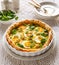 Quiche with with boiled eggs and leeks sprinkled with fresh lambs lettuce and dill served in casserole dish on a white table