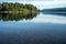 A quiet peaceful summer morning with view over crystal clear calm lake with pebbles in the bottom and forest reflected