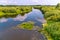 A quiet transparent river against a background of green vegetation and a blue sky