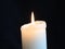 Quietly burning white candle on a black background
