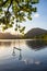 Quintessential beautiful English Summer landscape image of child`s rope swing over calm lake in Lake District during golden Summe