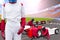 Race car driver posing in front of the pit stop with team maintaining technical service for a racing car during competition event