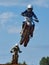 Racer on a cross-country motorcycle in sports equipment in flight after jumping on a springboard, against the blue sky