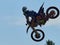 Racer on a cross-country motorcycle in sports equipment in flight after jumping on a springboard, against the blue sky