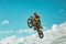Racer on motorcycle dirtbike motocross cross-country in flight, jumps and takes off on springboard against sky. Concept