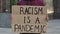RACISM IS A PANDEMIC on a cardboard poster in the hands of an African American rights activist. Closeup of poster and