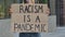 RACISM IS A PANDEMIC on a cardboard poster in the hands of female protester activist. Closeup of poster and hand. Stop