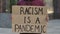 RACISM IS A PANDEMIC on cardboard poster in hands of male protester activist. Stop Racism concept, No Racism. Rallies