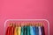 Rack with bright clothes on pink background. Rainbow colors