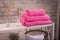 Rack with a stack of three pink carnation color towels and baskets with clean white towels and toilet decor near brick wall. Shelf