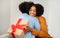Radiant African American woman with a bright smile hugs a man while holding a gift