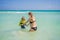 A radiant pregnant mother and her excited son share a tender moment on a serene, snow-white beach, celebrating