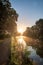 Radiant Sunrise: Sunlit Canal Reflecting Amidst Tranquil Trees