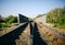 Rail tracks over the bridge in the green field. Railway transport industry. Empty road on summer day