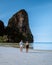 Railay Beach Krabi Thailand, couple walking in the morning on the beach with tropical cliffs and long tail boats on the