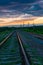 Railroad against the backdrop of sky and sunset clouds with green grass in the foreground. Beautiful sunset with orange