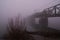 Railway Bridge Across River In Dark Foggy Winter Morning
