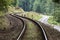 Railway curve and asphalt winding road in a green forest. Two communication and transport routes next to each other