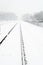 Railway in snowy rural landscape during snowfall.