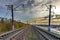 Railway at sunrise. Industrial landscape with railroad, colorful blue sky with red clouds, sun, trees and green grass