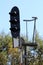 Railway tracks traffic light mounted on strong metal frame with safety fence surrounded with trees and clear blue sky