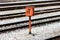 Railway trackside orange communication utility box mounted on metal pole and positioned on gravel between railway tracks