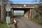 Railway tunnel leading to the road to the farmland, village in the distance and warning signs.