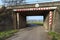 Railway tunnel leading to the road to the farmland, village in the distance and warning signs.