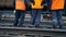 Railway workers are standing and looking at a passing train. Legs close-up. Worker in orange workwear