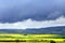 Rain clouds pull over rapeseed fields and mountains