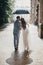 Rain drops on background of blurred stylish bride and groom walking under umbrella and kissing at old church in rain. Provence