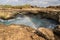 Rainbow above water at Devil`s Tear, Nusa Lembongan. Rocks in foreground. Cloudy sky.