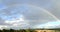 Rainbow across blue sky over green hills