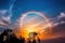 a rainbow appears in the sky over a tree line at sunset or dawn with clouds and trees in the foreground and a blue sky with white