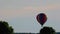 Rainbow colored hot air balloon ascends slowly to right firing propane in early morning soft light