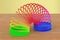 Rainbow colored plastic, slinky toy on the wooden table. 3D rend
