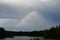 Rainbow on a dark stormy sky on summer day, over a dark lake in the forest, horizontal photo. The concept of peace and