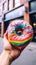 rainbow donut held in hand with street view, life style Authentic living