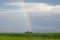 A rainbow extends skyward atop a green hill.