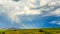 The rainbow glows in the sunlight against the background of dark clouds. Shadows of the sun move along the wheat fields