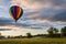 Rainbow hot-air balloon floats over farm field and trees at sunrise