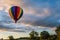 Rainbow hot-air balloon floats over farm field and trees at sunrise