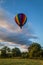 Rainbow hot-air balloon floats over trees at sunrise, portrait