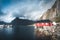 Rainbow ofer red houses rorbuer of Reine in Lofoten, Norway with red rorbu houses, clouds, rainy blue sky and sunny