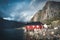 Rainbow ofer red houses rorbuer of Reine in Lofoten, Norway with red rorbu houses, clouds, rainy blue sky and sunny