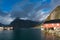 Rainbow ofer red houses rorbuer of Reine in Lofoten, Norway with red rorbu houses, clouds, rainy blue sky and sunny