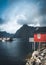 Rainbow ofer red houses rorbuer of Reine in Lofoten, Norway with red rorbu houses, clouds, rainy blue sky and sunny