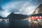 Rainbow ofer red houses rorbuer of Reine in Lofoten, Norway with red rorbu houses, clouds, rainy blue sky and sunny