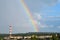 A rainbow over the forest and the outskirts of the city against the sky. Roofs of houses and a striped chimney in the foreground.